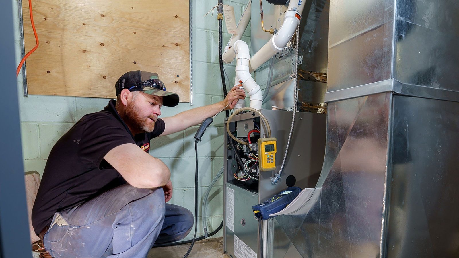 Technician testing a gas furnace in a utility room with a meter