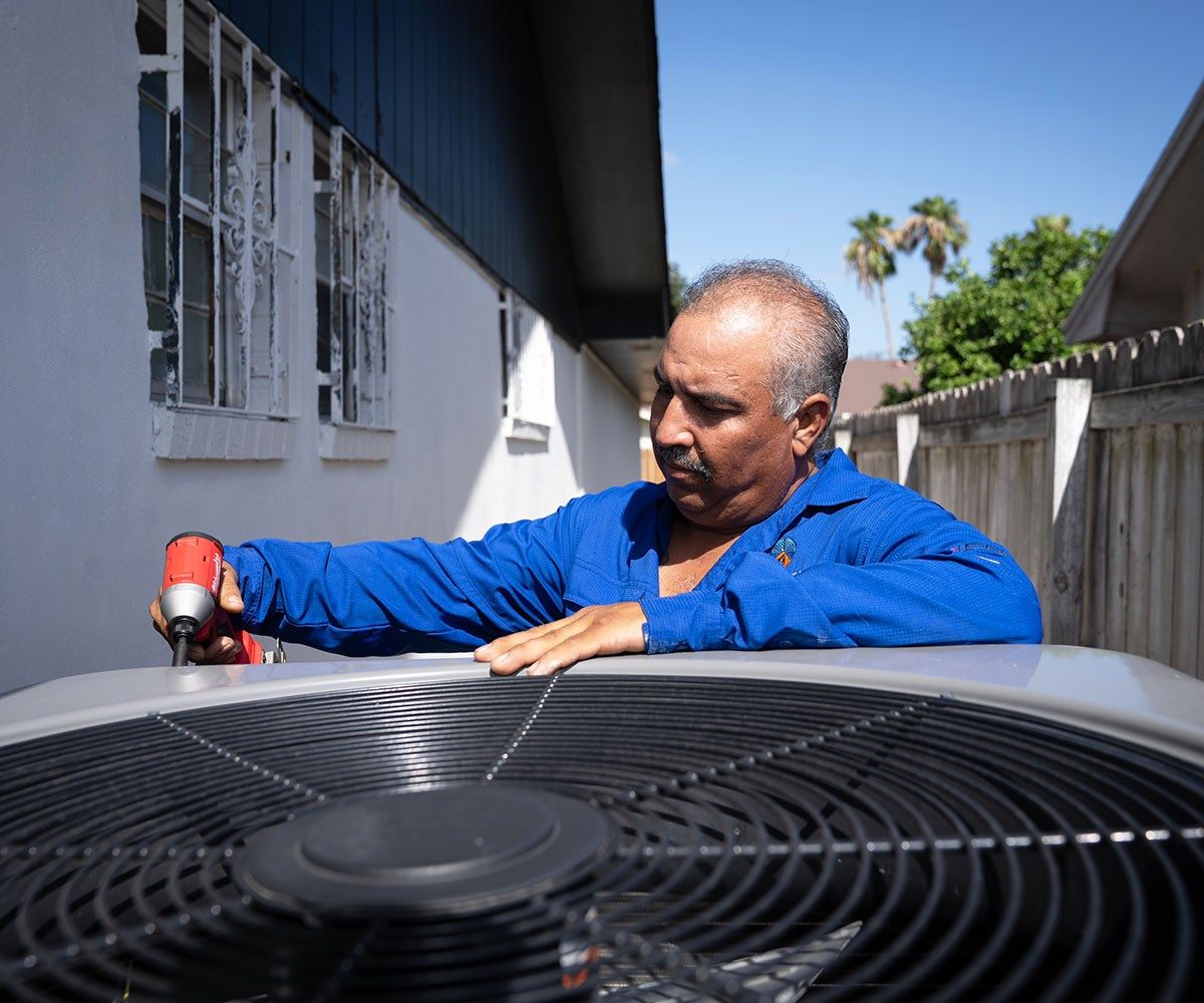 Technician opening the top of an outdoor air conditioning unit beside a house