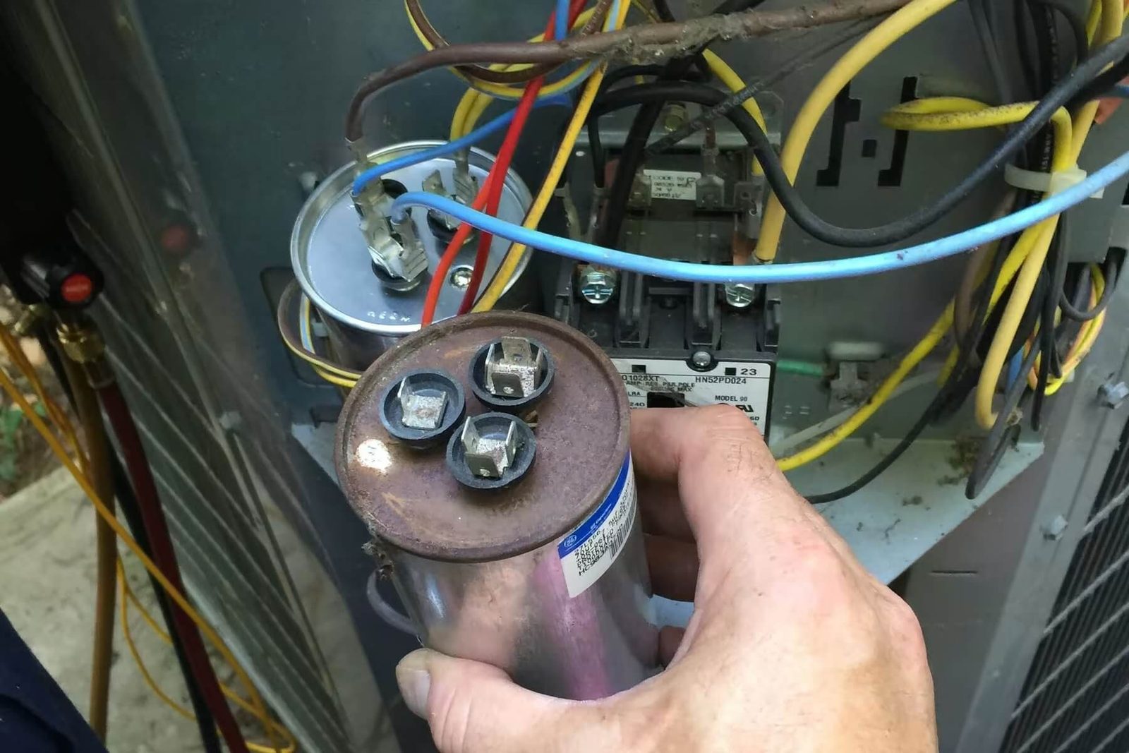 Technician holding a run capacitor removed from an air conditioner control panel
