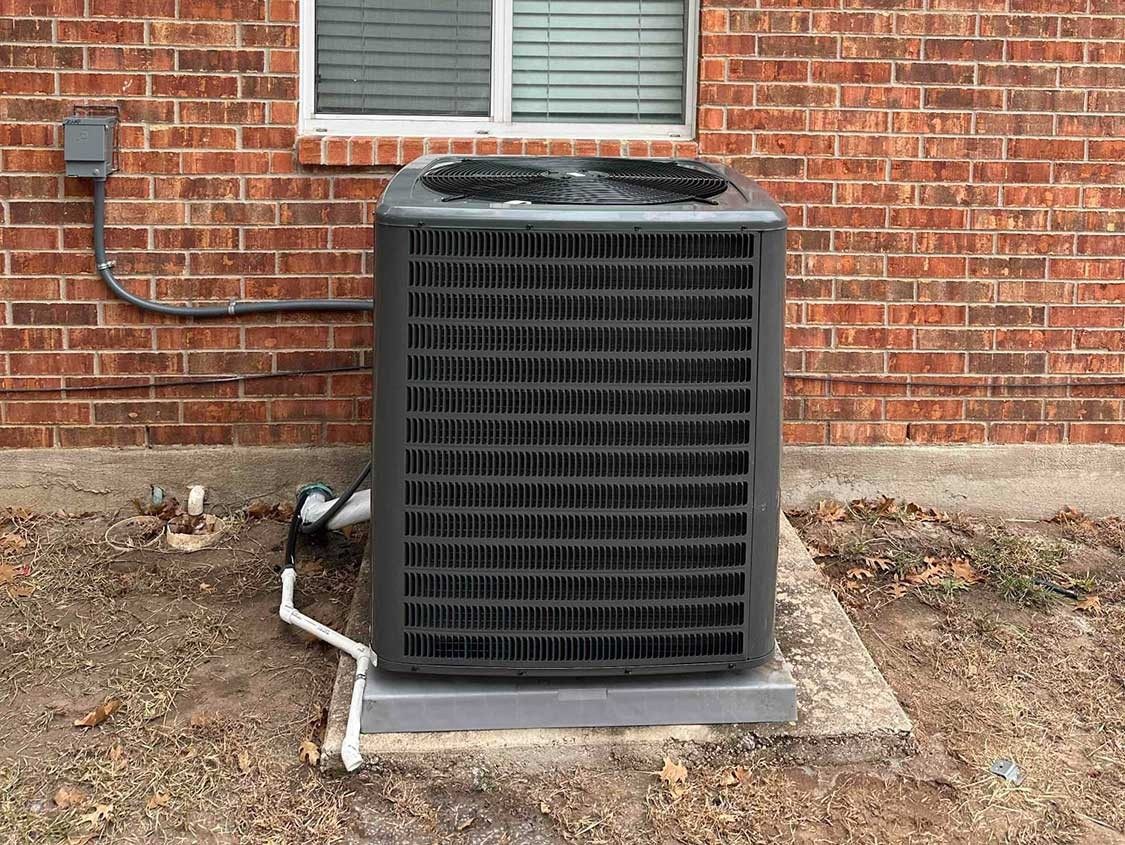 New outdoor air conditioning unit on a pad beside a red brick house